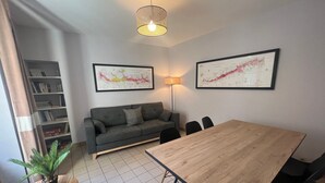 Een moderne woonkamer met een grijze bank, een houten eettafel en twee inlijstte kaarten aan de muur.
