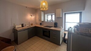 Een moderne keuken met een vaatwasser, spoelbak en een inbouwoven. Er is een raam dat zorgt voor natuurlijk licht, en een hanglamp boven het aanrecht.