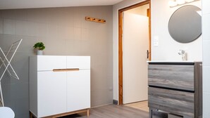 Een moderne badkamer met een wit kastje, een houten deur, een spiegel en een handdoekhouder.