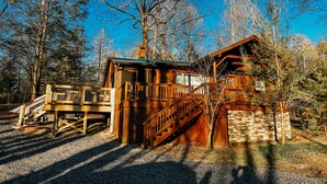Une cabane en bois avec un escalier menant à une terrasse, le tout entouré d’arbres.