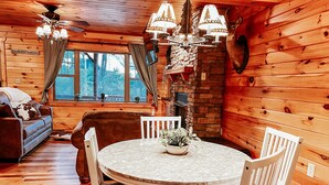 L’intérieur chaleureux d’un chalet, avec un décor en bois, une table à manger ronde entourée de chaises, un canapé et une cheminée.