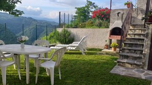 Eine Terrasse mit einem runden Tisch und Stühlen, eine Steintreppe und Blick auf Berge.