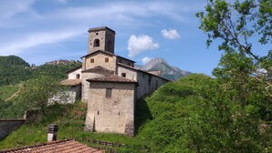 Eine steinerne Kirche mit einem Glockenturm, umgeben von üppigem Grün und Bergen im Hintergrund.