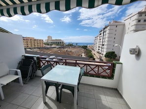 A balcony with a table and chairs, overlooking a construction site and buildings.