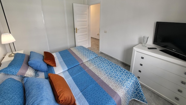 A bedroom with a bed, pillows, a TV, a dresser, and a door. - Victoria Court II (Los Cristianos)
