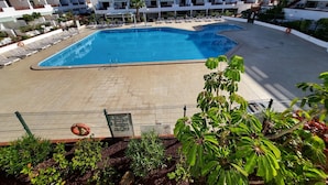 A swimming pool surrounded by lounge chairs, with a view of multi-story buildings in the background. - Victoria Court II (Los Cristianos)
