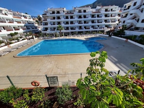 A swimming pool surrounded by lounge chairs and a multi-story building with balconies.