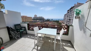 A balcony with a table and chairs, overlooking a cityscape and the sea. - Victoria Court II (Los Cristianos)