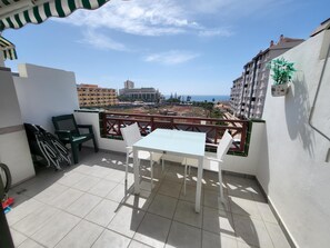 A balcony with a table and chairs, a view of the cityscape, and a potted plant.