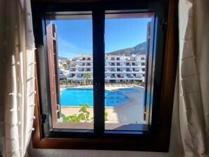 A view from a window of a hotel with a pool, multiple balconies, and a mountain in the background. - Victoria Court II (Los Cristianos)