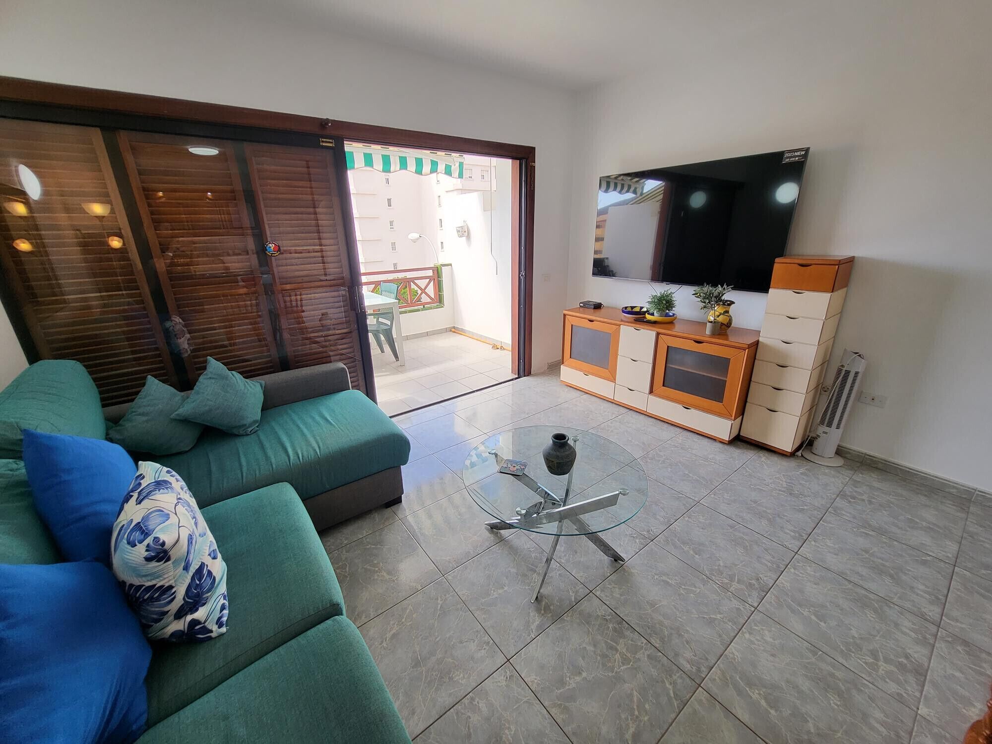 Una sala de estar con un sofá verde, una mesa de centro de vidrio, un televisor y una puerta corrediza que da a un espacio exterior.