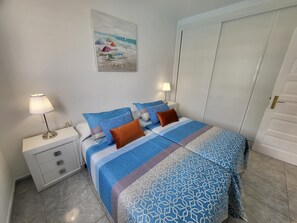 A bedroom with a bed, two bedside tables, a lamp, a painting, and a door.