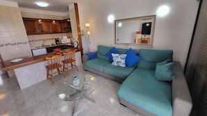 A modern living space with a kitchen, dining area, and a large sofa with blue cushions. - Victoria Court II (Los Cristianos)