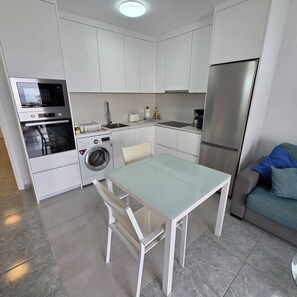 A compact kitchen with a built-in oven, microwave, washing machine, and a refrigerator. - Victoria Court II (Los Cristianos)
