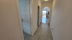 A hallway with a white door, a tiled floor, and a view of a balcony. - Victoria Court II (Los Cristianos)