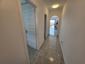 A hallway with a white door, a tiled floor, and an arched doorway leading to a balcony with a view.