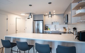 A modern kitchen with a large island, stainless steel appliances, pendant lighting, and bar stools. - Alpine Dream by Revelstoke Vacations (Revelstoke)