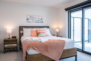 A bedroom with a wooden bed, white bedding, a pink blanket, and a nightstand with a lamp. - Alpine Dream by Revelstoke Vacations (Revelstoke)