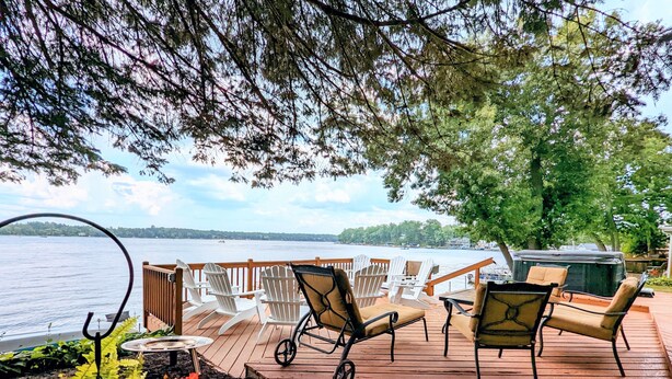 A wooden deck with outdoor seating, a grill, and a view of a lake.
