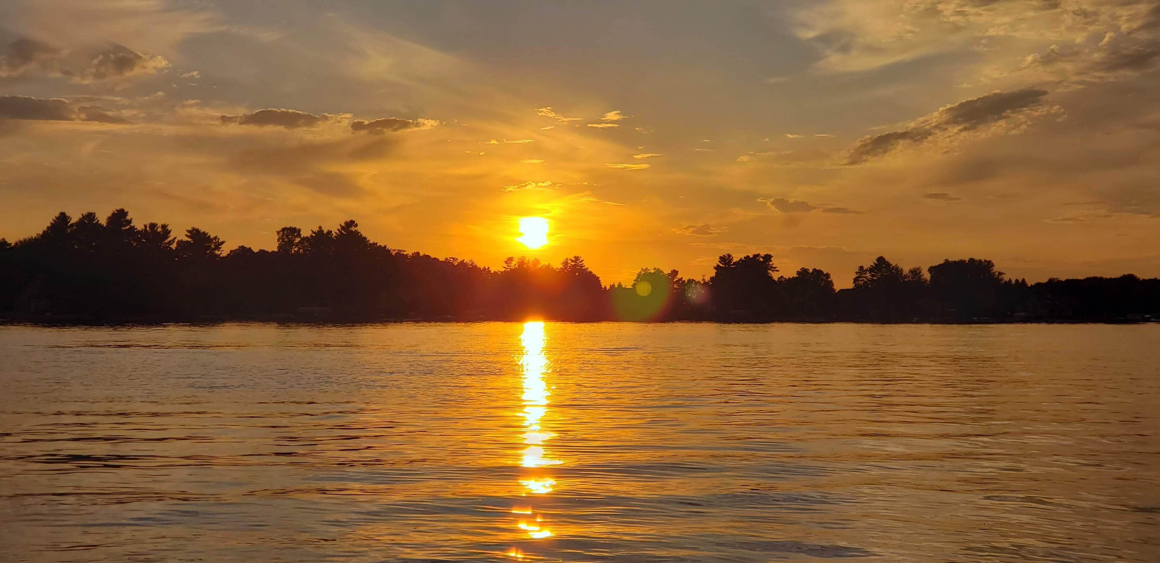 A sunset over a calm body of water with a silhouette of trees in the background.