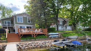 A dock leading to a small docked boat, a wooden deck, and a house with a porch.