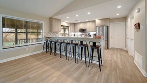 A modern kitchen with a central island, bar stools, and a large window with blinds. - Longhorn River Ranch (Seguin)