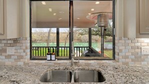 A kitchen with a double sink, a window overlooking a garden, and a view of a patio area. - Longhorn River Ranch (Seguin)