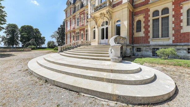 Ein prächtiges Gebäude mit einem zentralen Eingang, einer zur Auffahrt führenden Treppe und einem gepflegten Garten.