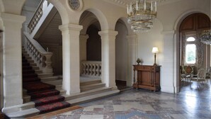 Eine prachtvolle Eingangshalle mit Treppe, Rundbögen, einem Chandelier und einem Holzkonsolentisch mit Lampe.