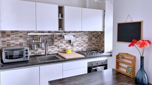 Une cuisine moderne avec des armoires blanches, un pare-feu en carreaux, une cuisinière à gaz, un grille-pain et une planche à découper en bois.