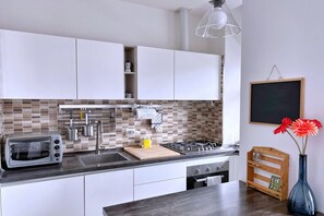 Una cocina moderna con armarios blancos, salpicadero de azulejos, estufa a gas, tostadora y tabla de cortar de madera.