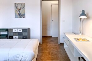 A hotel room with a bed, a desk, a lamp, a painting, and a wardrobe.