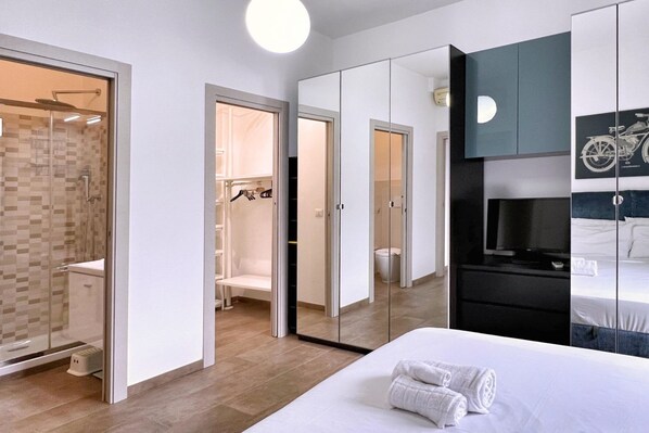Una habitación de hotel moderna con una cama grande, televisión, espejo y vestidor.