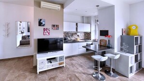 Une cuisine moderne avec des meubles blancs, un pare-feu en carrelage et un îlot central. On y trouve un coin repas avec des tabourets de bar blancs et une petite table.