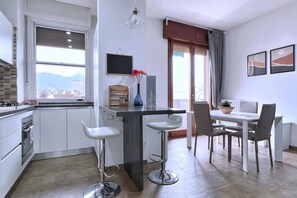A modern kitchen with a dining area, featuring a bar stool, a dining table with chairs, a TV, and a window with a view.