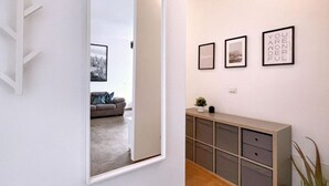 Un couloir avec un mur recouvert de miroirs qui reflète un salon, une console sur laquelle sont posées des photos encadrées et une plante.