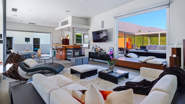 A modern living room with a large TV, comfortable seating, a kitchen area, and a view of the outdoors. - 25% Off Sep 3-6 Perfect 4 Families -Pool, Jacuzzi* (Palm Springs)