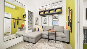 A modern living room with a grey sectional sofa, a small wooden table, and a large mirror reflecting the room. - 25% Off Sep 3-6 Perfect 4 Families -Pool, Jacuzzi* (Palm Springs)
