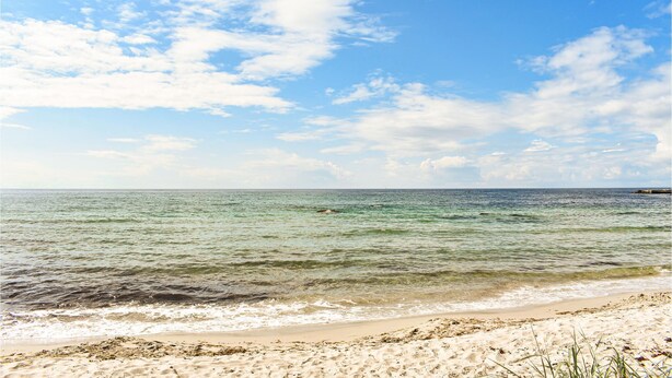 A beach with clear water, a sandy shore, and a partly cloudy sky.