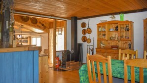 A wooden interior with a dining area, a kitchen with a stove, and a wooden cabinet with dishes.