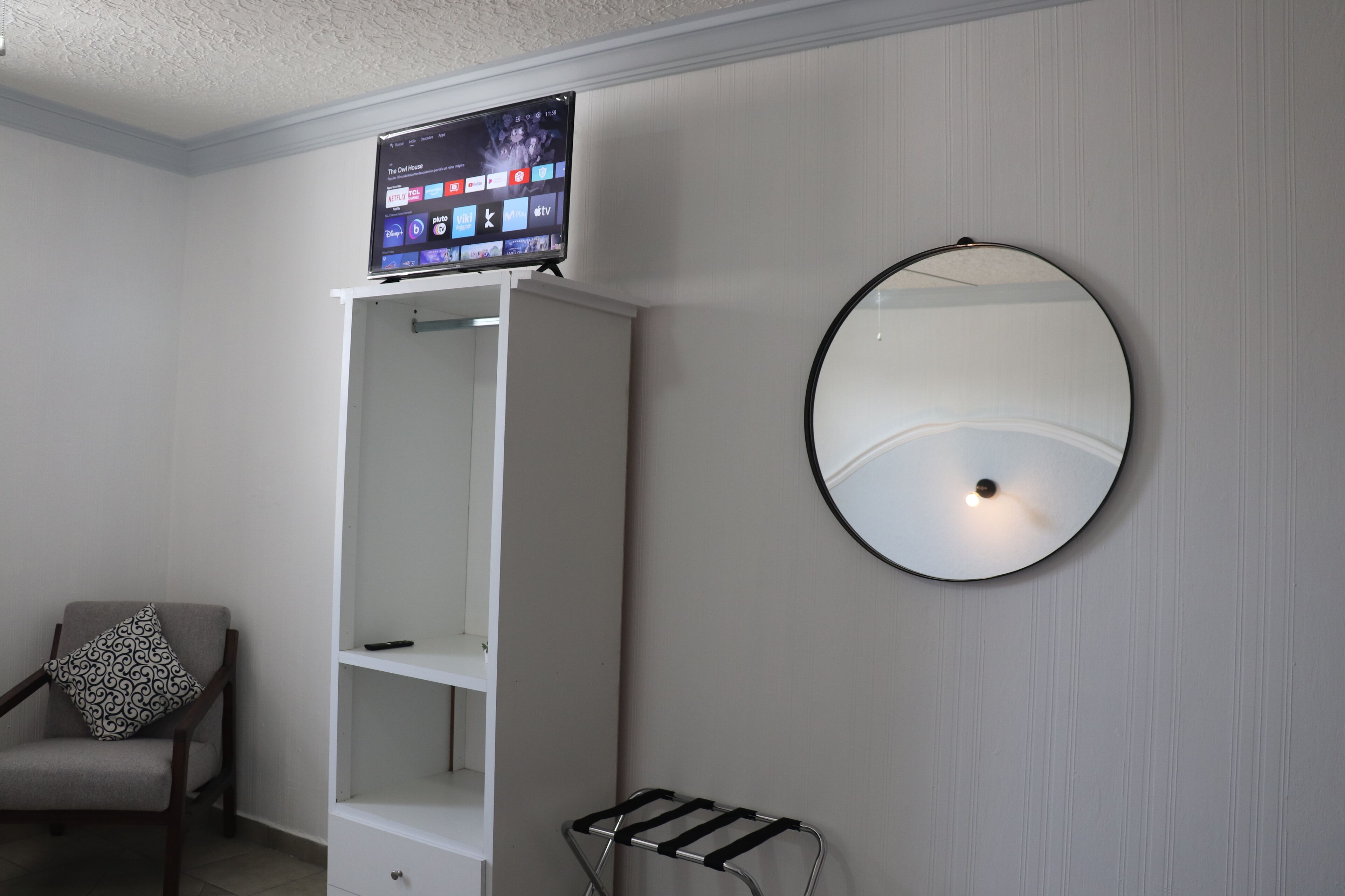 A room with a TV on a stand, a wardrobe, a mirror, and a chair.