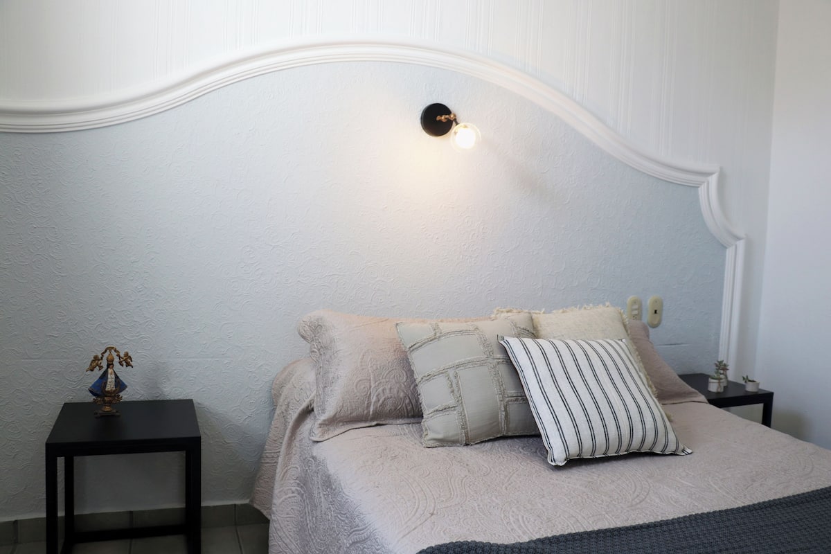 Une chambre à coucher comprenant un lit, une table de chevet, une lampe et un luminaire fixé au mur.