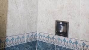 Neliönmuotoinen, rei’itetty suihkupää, metallinen kahva ja pieni neliönmuotoinen viemäri laatoitetussa seinässä.