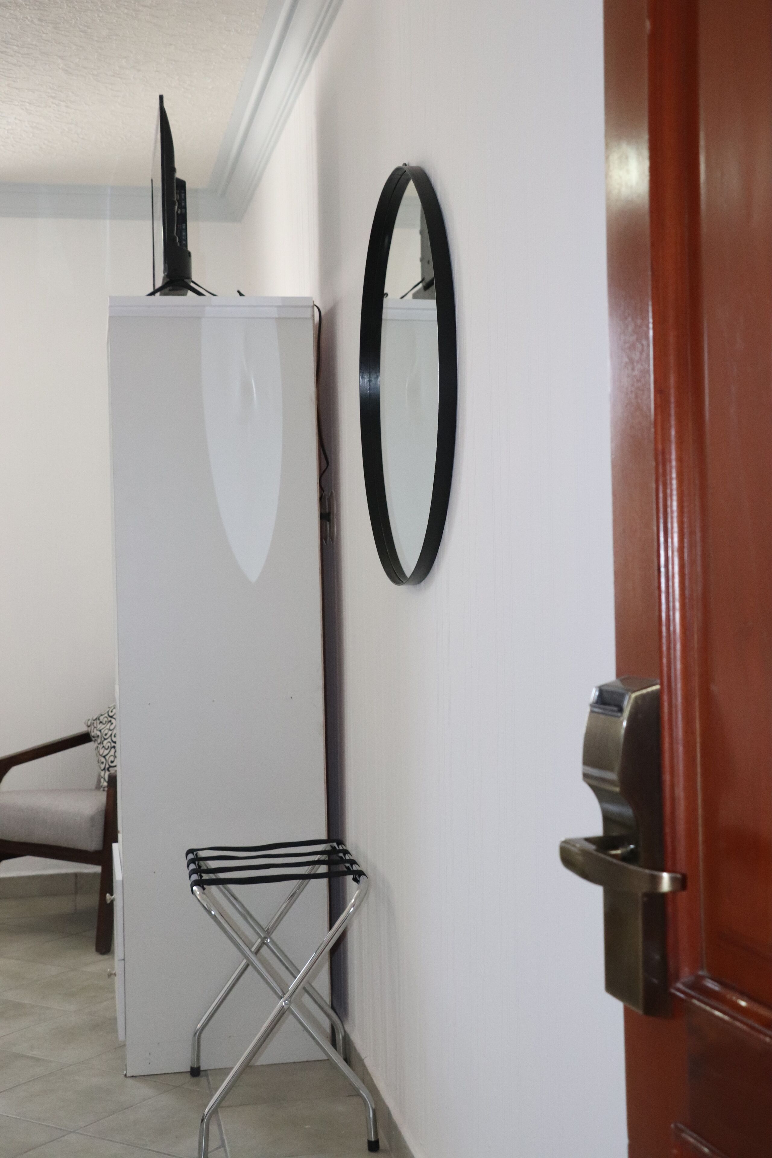 A hallway with a white refrigerator, a metal drying rack, a mirror, and a wooden door.