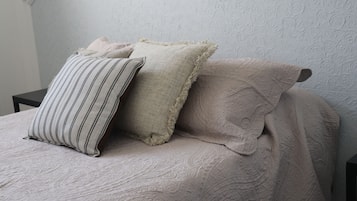Een bed met een geribbelde beige sprei en drie kussens, waarvan één gestreept, één met een ruwe textuur, en één met een bloemenprint.