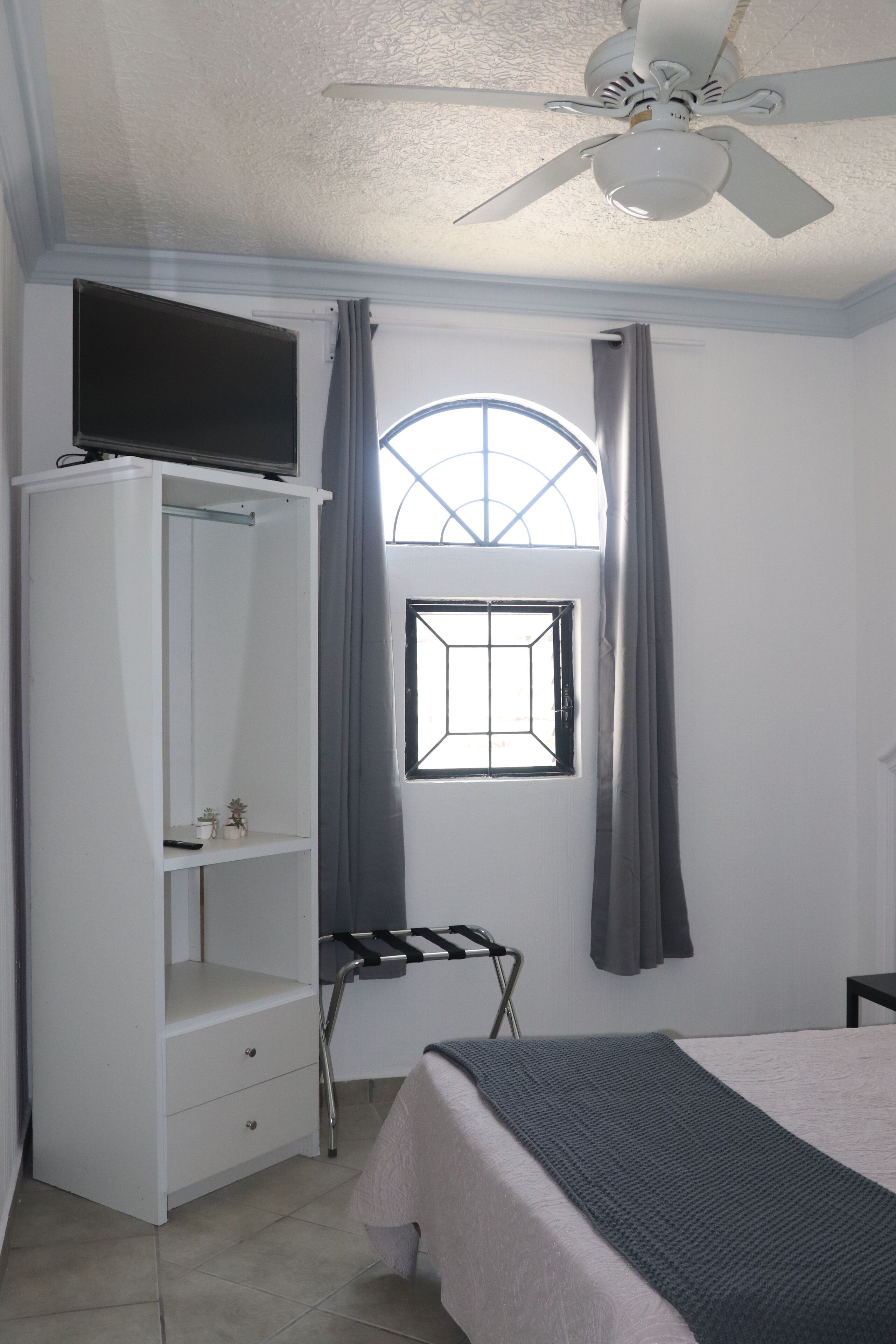 A bedroom with a bed, a wardrobe, a ceiling fan, a window, and a small table.