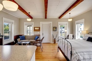 A spacious room with a large bed, a sofa, and a dining area. There are two doors leading to other rooms, and the room has wooden beams on the ceiling.