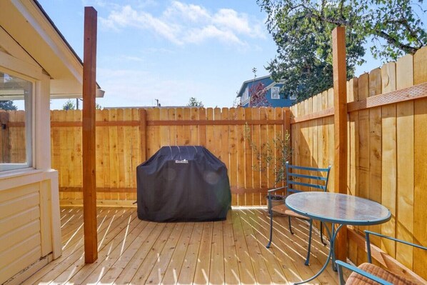 A wooden deck with a barbecue grill, a table, and chairs.