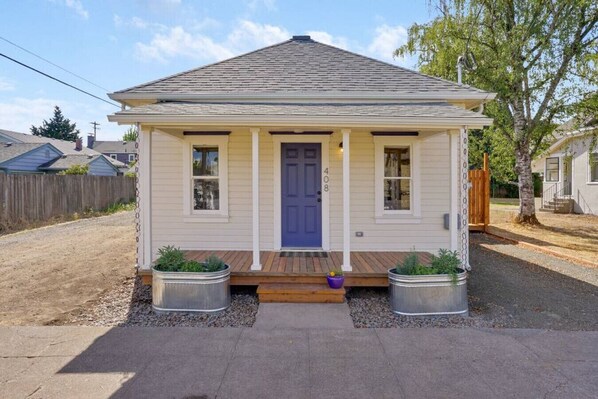 A single-story house with a front porch, two potted plants, and a blue door.