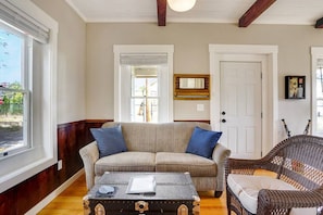 A living room with a beige sofa, two blue cushions, a wicker chair, a wooden coffee table, and a white door.